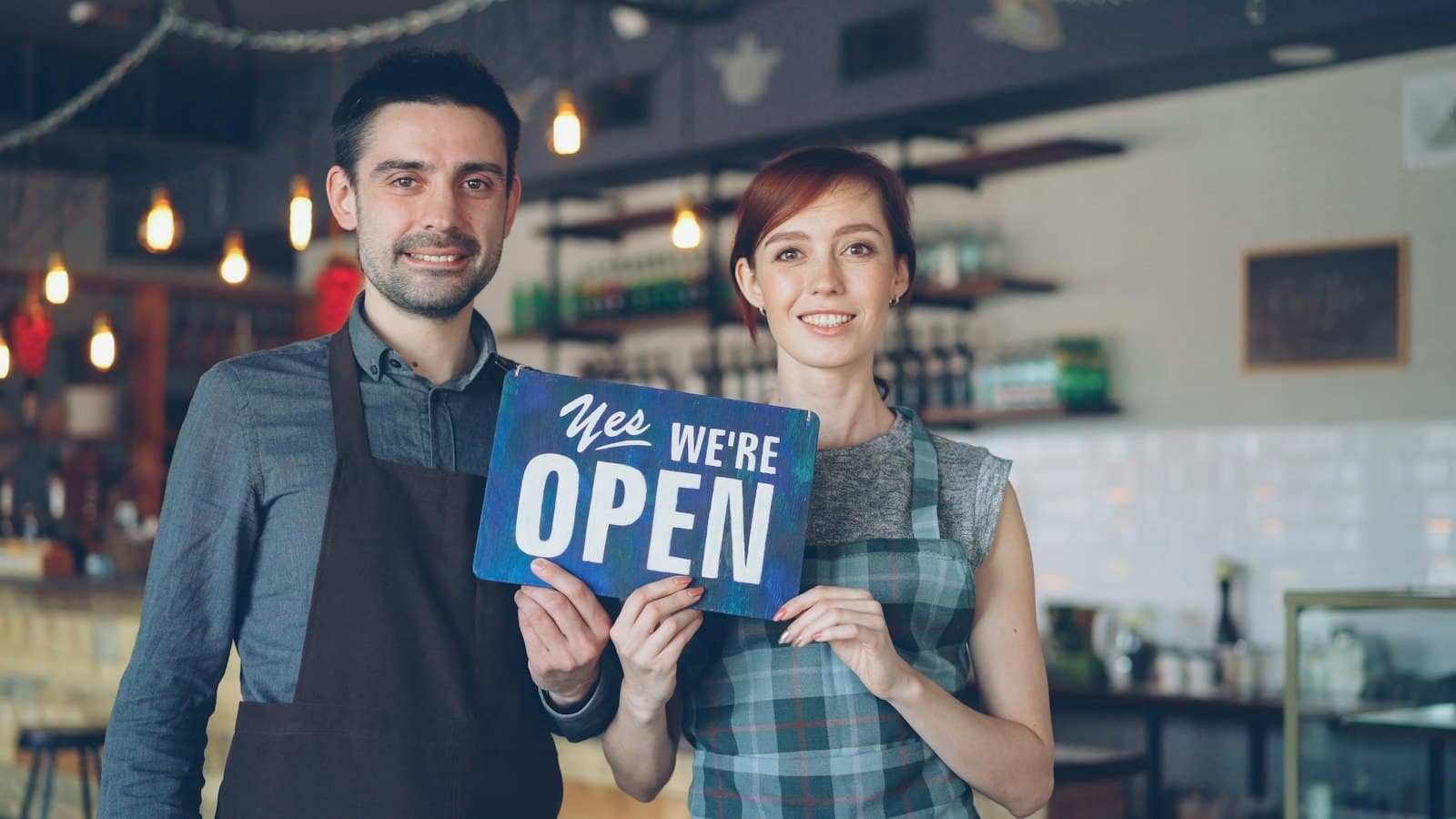 Two smiling shop owners holding an Open sign